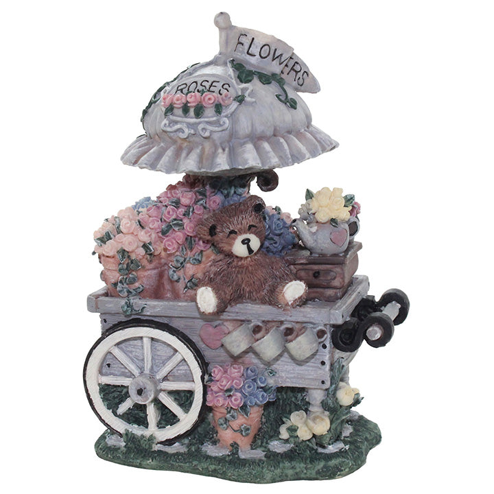 Decorative figurine of a teddy bear with flowers and a cart on a white background