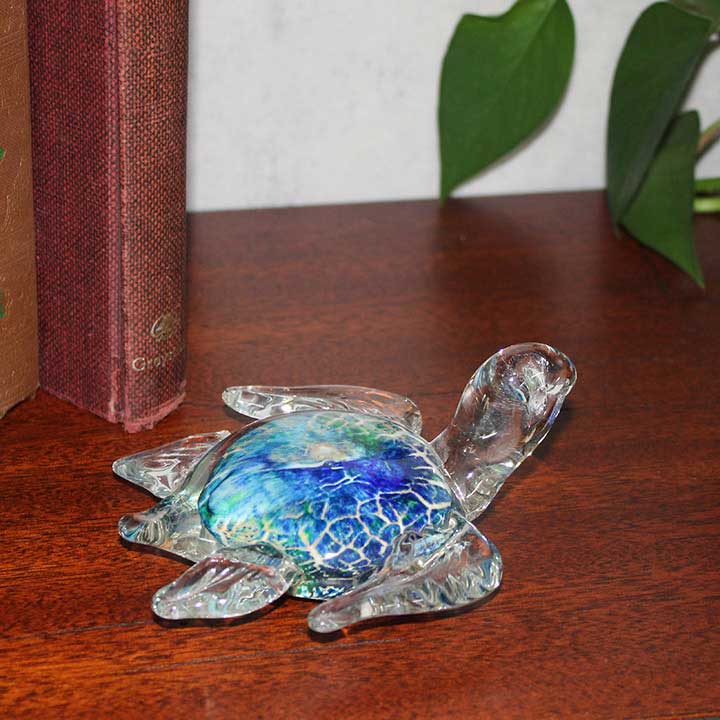 image of blown glass sea turtle with blue and green shell displayed on a shelf with books and plant